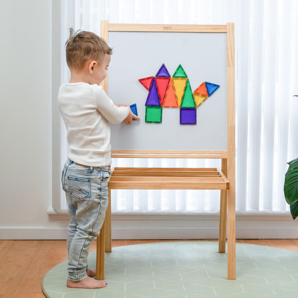 Child playing with Connetix Rainbow Mini Pack - 24 Piece Set colorful magnetic shapes on a wooden easel.