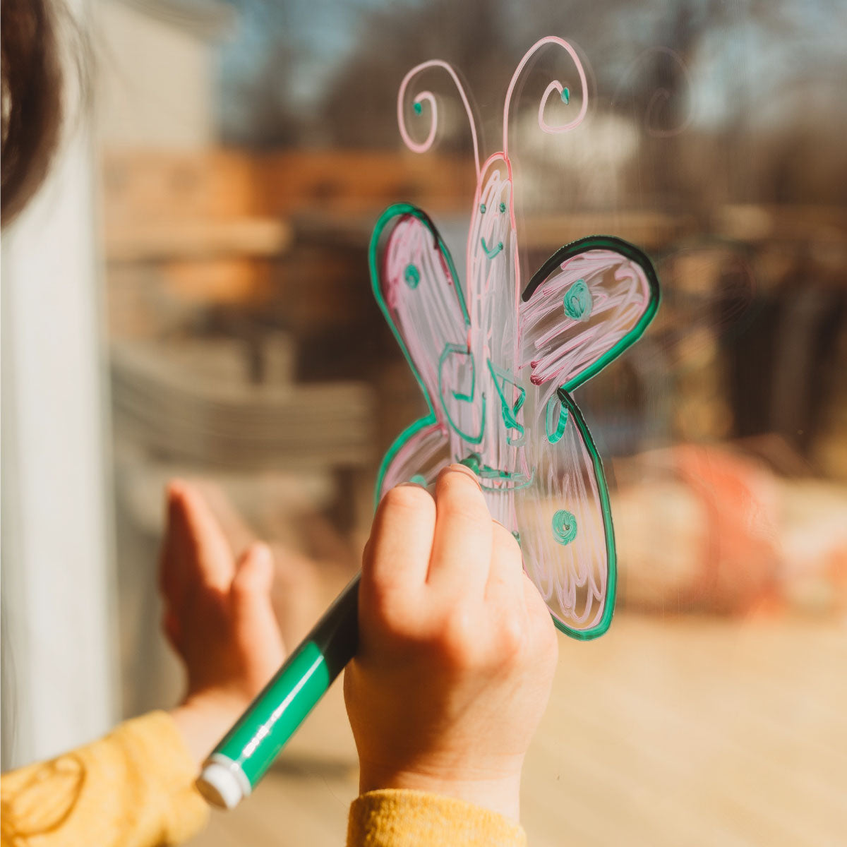 The Pencil Grip Co Magic Stix Washable Acrylic Markers child drawing a butterfly on glass.