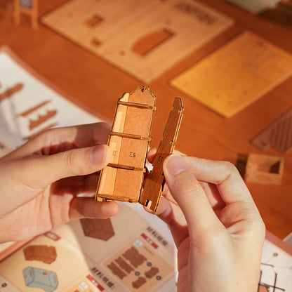 Hands assembling pieces of the Corner Bookstore, DIY Miniature House Kit. 