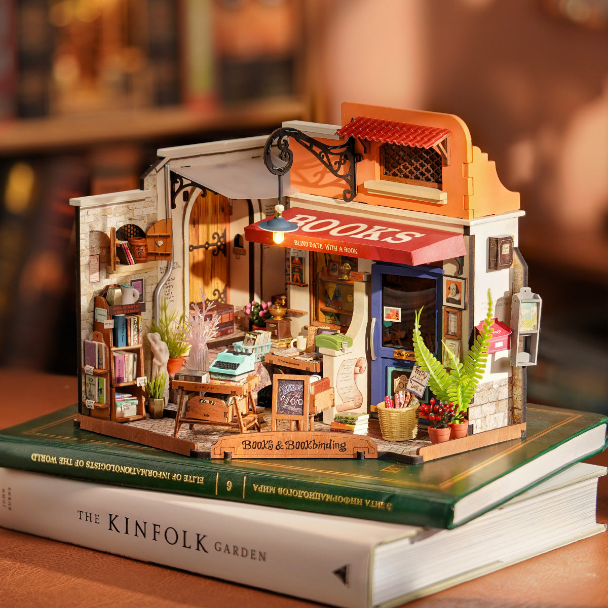 Completed Corner Bookstore DIY Miniature House Kit with warm LED lights on, sitting atop books. 