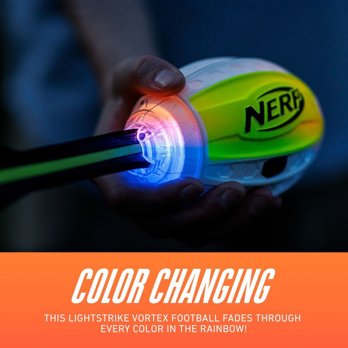 A hand holds a Nerf lightstrike vortex football showing a color-changing rainbow effect. The bottom of the image features an orange banner with white text that reads 'COLOR CHANGING' and 'THIS LIGHTSTRIKE VORTEX FOOTBALL FADES THROUGH EVERY COLOR IN THE RAINBOW!'.