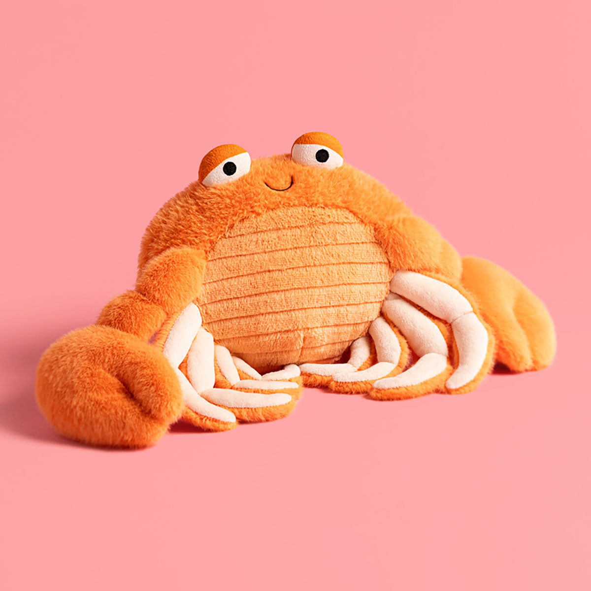 Jellycat Pinchsnap Crab plush orange crab toy with white claws and a smiling face, photographed against a solid pink background.