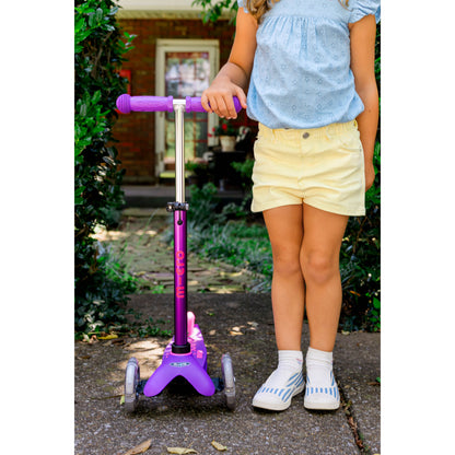 Child standing next to a Micro Kickboard Mini Deluxe Scooter LED Wheels - Purple & Pink